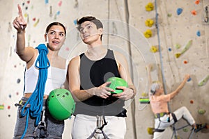 Happy excited young male and female visitors discussing upcoming climbing artificial training rock wall in indoor