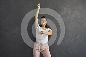 Happy excited young woman dancing gangnam style against dark grey studio background
