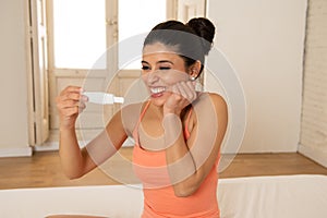 Happy, excited young woman holding a pregnancy test looking at the positive result in joy