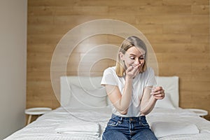 Happy, excited young woman holding a pregnancy test looking at the positive result in joy.