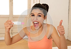 Happy, excited young woman holding a pregnancy test looking at t