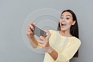 Happy excited young woman playing video games on cell phone
