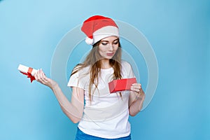 Happy excited young woman in santa claus hat with gift box on blue background