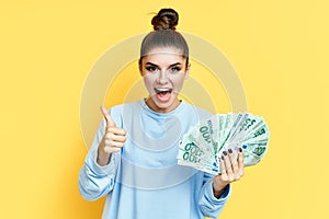 Happy excited young woman showing money banknotes with thumbs up