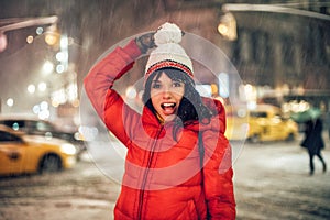 Happy exited woman having fun on city street of New York under the snow at winter time wearing hat and jacket.