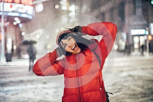 Happy exited woman having fun on city street of New York under the snow at winter time wearing hat and jacket.