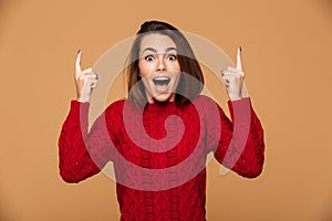 Happy exited young woman in red sweater pointing up with two fin