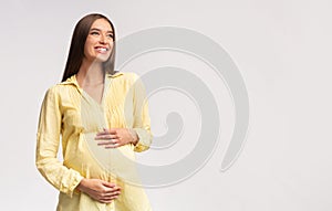 Happy expectant lady touching pregnant belly, studio shot
