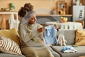 Happy Expectant Mother Looking at Baby Clothes in Hands