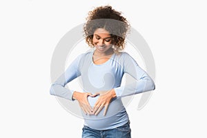 Happy expectation. Black pregnant woman forming heart shape on belly