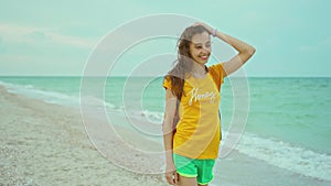 happy expression woman with blowing hair wearing yellow t-shirt walking and having fun on ocean beach, raising hands.