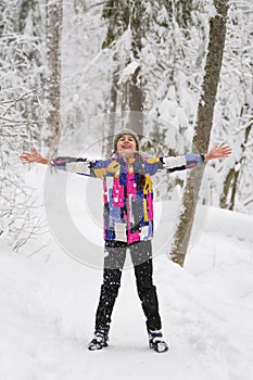 Happy expressive teenage girl enjoying the first snow standing with open arms in winter