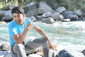 A happy face guy sitting near river lake and enjoying the manali road trip