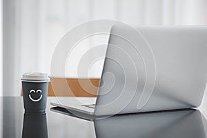 Happy face icon on coffee paper cup with laptop on table