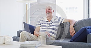 Happy, face and senior man on a sofa laughing, confident and positive attitude at home with good mood. Smile, portrait
