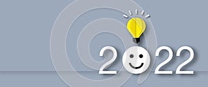 Happy face in the year 2022 with light bulb on grey background. Concept for innovative business vision or resolution.