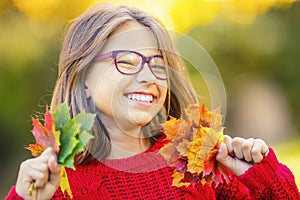 Happy fall girl smiling and joyful holding autumn leaves. Beautiful young girl with maple leaves in red cardigan