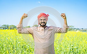 Happy famer showing stroing gesture using two hands at farmland by looking at camera - conept of confident, agro