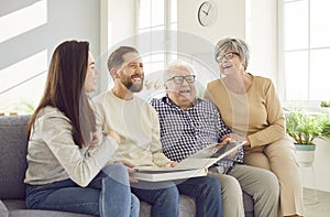 Happy family, aging old parents and adult children watching photo album to remember funny childhood