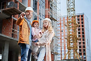 Happy family with apartment keys standing at construction site.