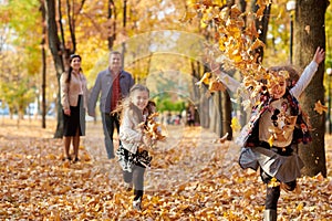 Happy family is in autumn city park. Children and parents running with leaves.. They posing, smiling, playing and having fun.