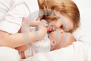 Happy family. baby and mother play, kiss, tickle, laugh in bed