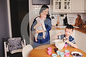 Happy family baking together in modern white kitchen. Mother, son and baby daughter cooking in cozy weekend morning