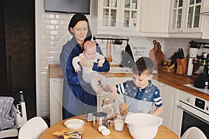 Happy family baking together in modern white kitchen. Mother, son and baby daughter cooking in cozy weekend morning