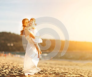 Happy family at beach. mother hugging baby daughter at sunset