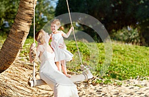 Happy family at beach. mother shook child on swing in summer