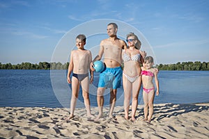 A happy family on the beach.  People having fun on summer holidays.  Father, mother and children against the blue river and sky