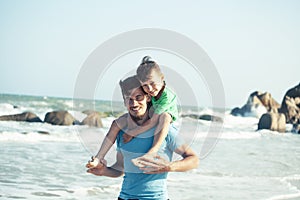 Happy family on beach playing, father with son walking sea coast, rocks behind smiling taking vacation