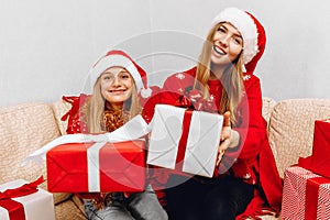 Happy family  beautiful mother and her little daughter in Santa Claus hats  are sitting at home on the couch with Christmas gifts