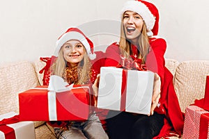 Happy family  beautiful mother and her little daughter in Santa Claus hats  are sitting at home on the couch with Christmas gifts