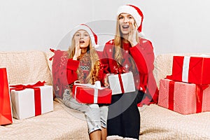 Happy family  beautiful mother and her little daughter in Santa Claus hats  are sitting at home on the couch with Christmas gifts