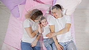 Happy family in bed, mom, son and dad are kissing and hugging together.