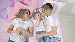 Happy family in bed, mom, son and dad are kissing and hugging together.