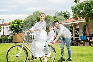 Happy family with bicycle outdoors on summer day, Asian father and mother with daughter enjoying riding a bike outdoors in a park