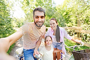 Happy family with bicycles taking selfie in summer