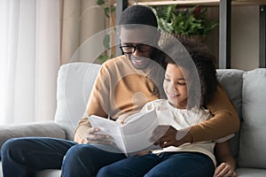 Happy family black father and kid daughter reading story book