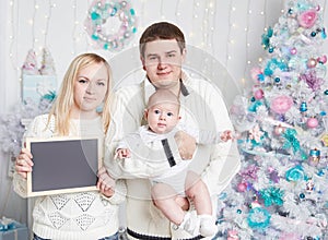 Happy family with a blank card while standing near the Christmas tree