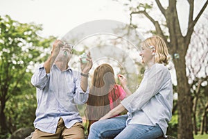 Happy family blow soap bubbles in park.