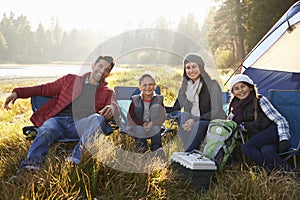 Happy family on a camping trip sit by tent looking to camera