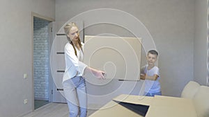 A happy family with cardboard boxes in a new house on the day of moving. Little son helps mom with a big box, mortgage