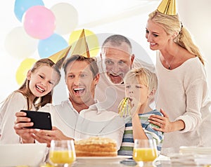 A happy family celebrating a birthday with a party, wearing hats and taking a selfie using a phone. Mature man taking a
