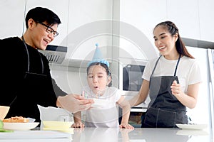 Happy family celebrating daughter girl birthday at kitchen together, father holding cake with candles for child kid to blow,