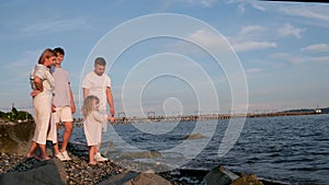 Happy family celebrating little girl's birthday on the seashore mom brings a box with cake girl opens a gift dad mom