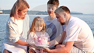 Happy family celebrating little girl's birthday on the seashore mom brings a box with cake girl opens a gift dad mom