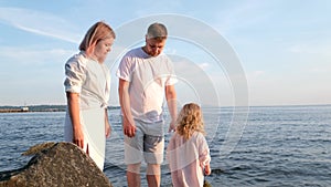 Happy family celebrating little girl's birthday on the seashore mom brings a box with cake girl opens a gift dad mom