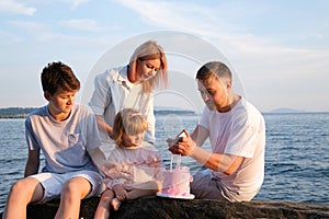 Happy family celebrating little girl's birthday on the seashore mom brings a box with cake girl opens a gift dad mom